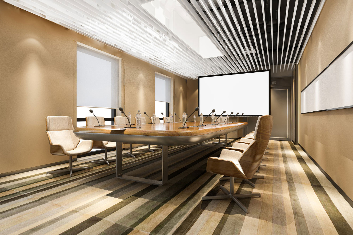 Modern boardroom with a long wooden table, beige chairs, and multiple microphones facing a blank presentation screen at the far end.
