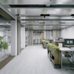 Open-plan office with white desks, grey chairs, and potted plants; glass-walled meeting room visible in the back.